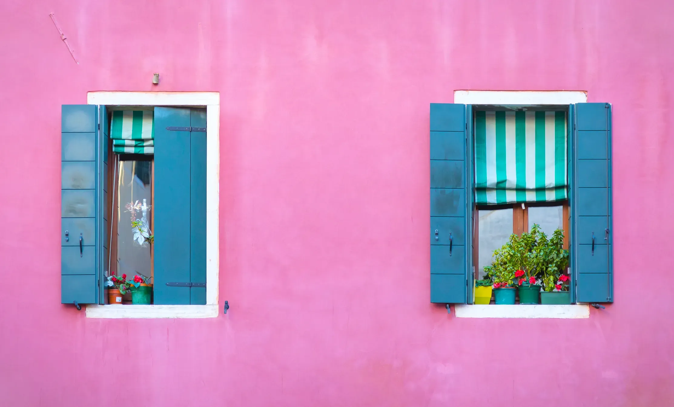Fachada de casa da cor rosa e janelas azuis.