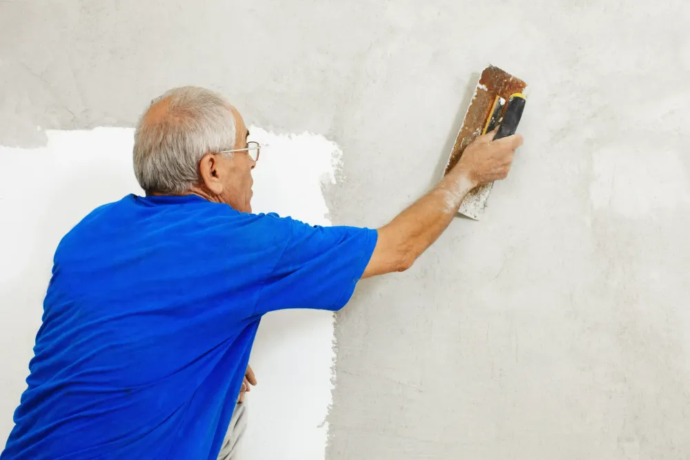 Homem aplicando com uma desempenadeira a massa acrílica na parede. 