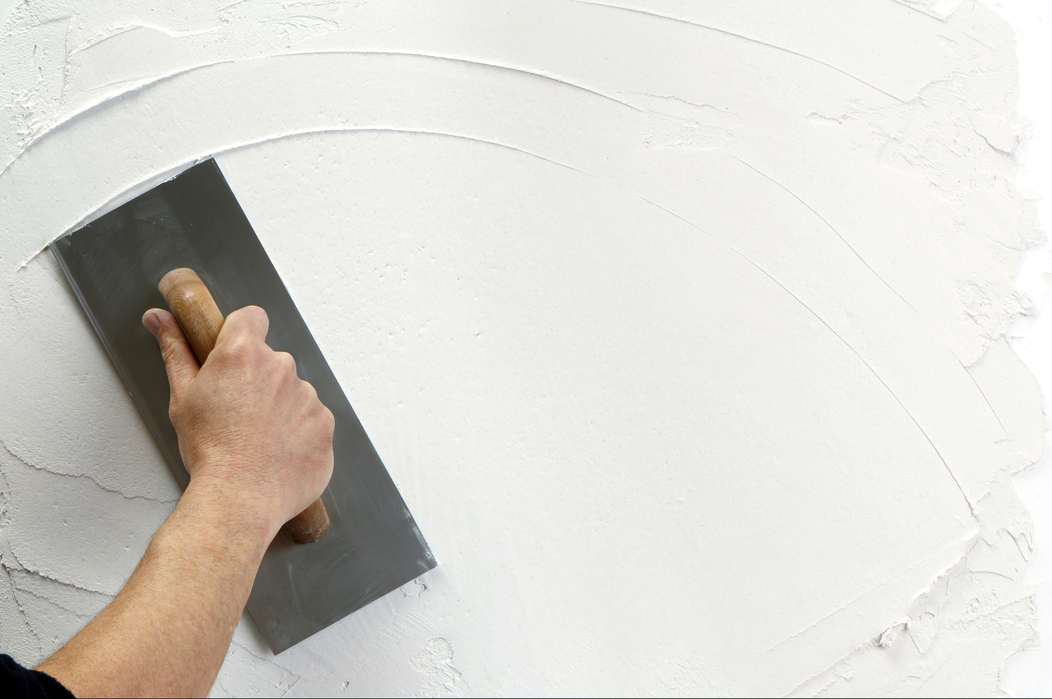 Mão aplicando massa acrílica e nivelando a superfície da parede.