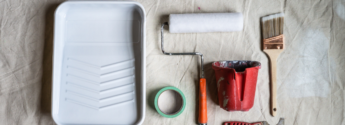 Materiais para pintura colocados lado a lado: bandeja, fita crepe, rolo de pintar, entre outros.