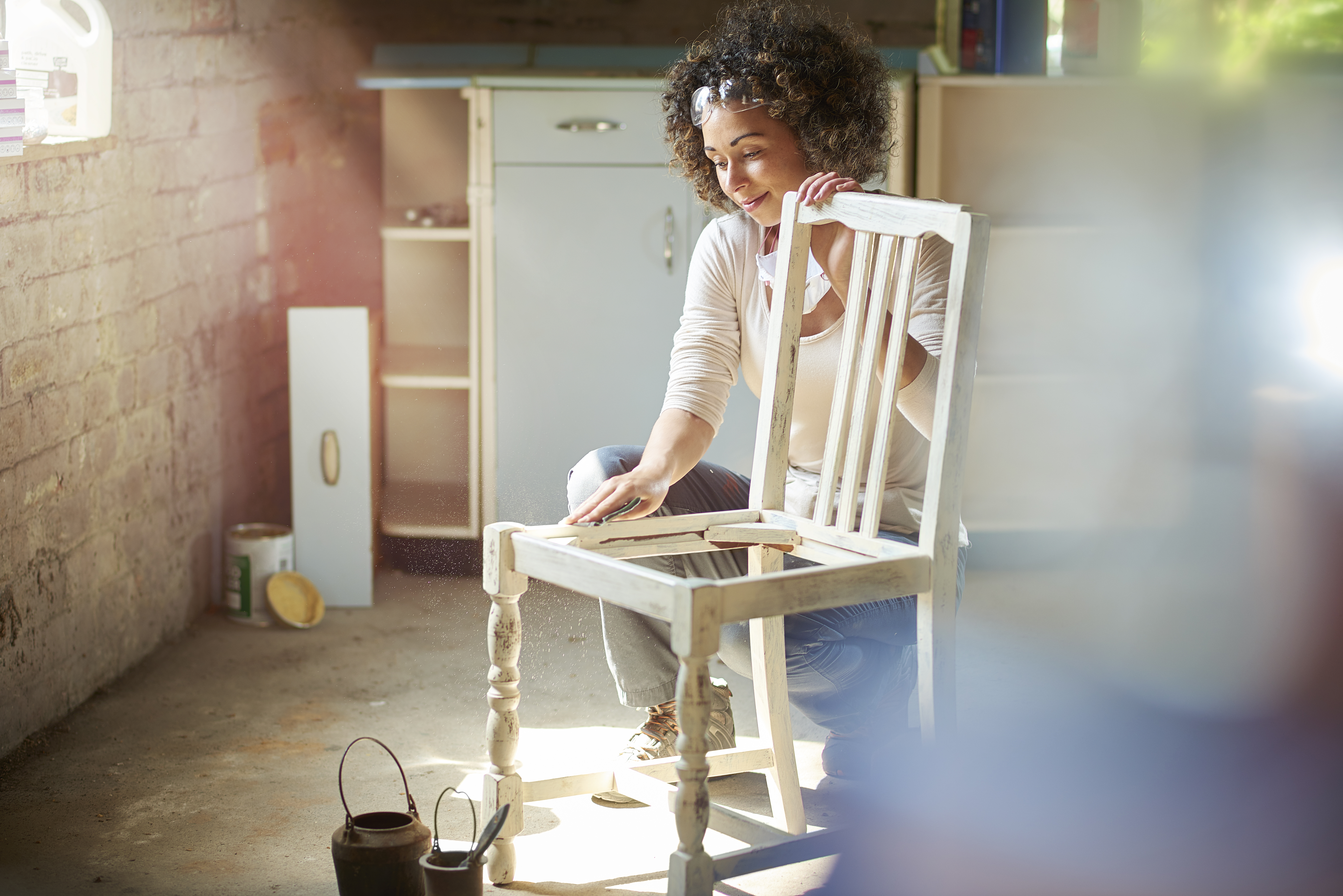 Mulher lixando cadeira de madeira, preparando-a para a aplicação do esmalte.