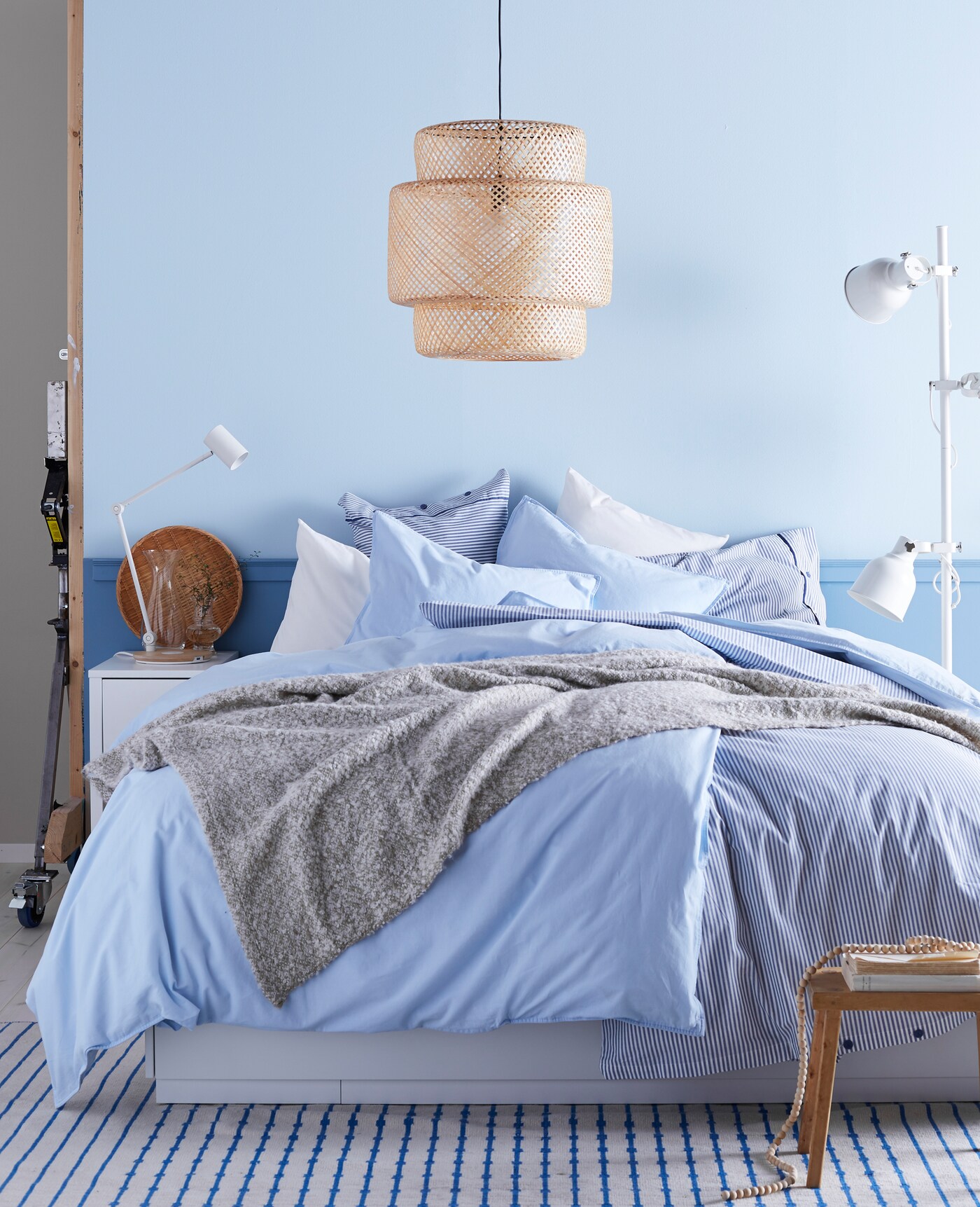 Quarto de casal com parede pintada de azul claro. A cama possui mantas e cobertores na cor azul.