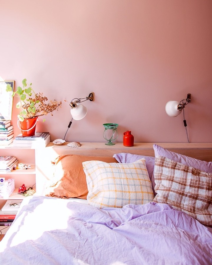 Quarto de casal com parede pintada de rosa chiclete. A cama possui roupa de cama em tom de azul.