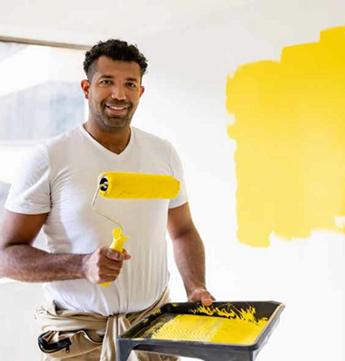 Homem segurando bandeja com tinta laranja na frente da parede que está pintando.